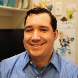 Photo of Zachary K. Watkins smiling and wearing a light blue buttoned shirt.